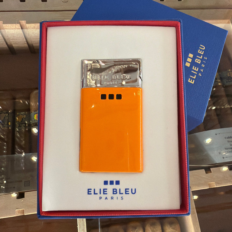 An orange Elie Bleu Paris cigar lighter in its original white box with a red border, displayed on top of a blue Elie Bleu Paris box in a cigar humidor.