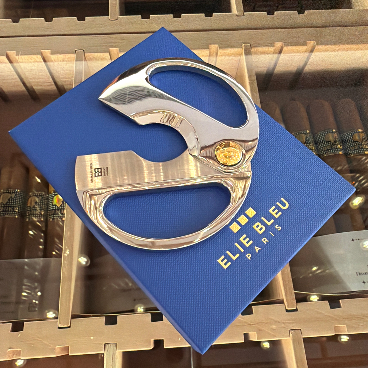 HAMILTON ELIE BLEU round cigar cutter with polished silver handles and a gold button resting on a blue gift box.