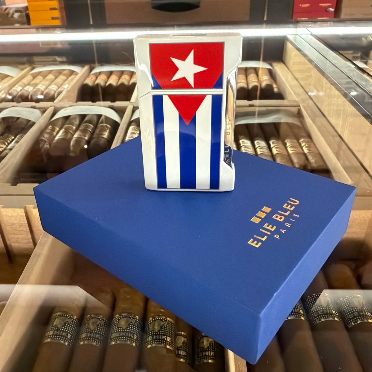 HAMILTON ELIE BLUE J-12 flat flame lighter featuring a Cuban flag design, displayed on a blue gift box in a humidor.